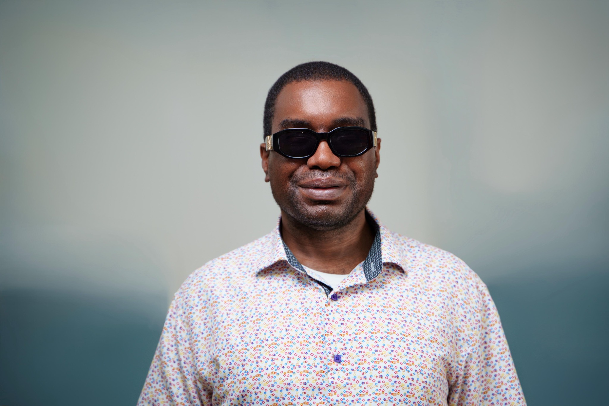Professional portrait of Kevin E. Cartwright wearing dark glasses and a patterned shirt, smiling warmly.