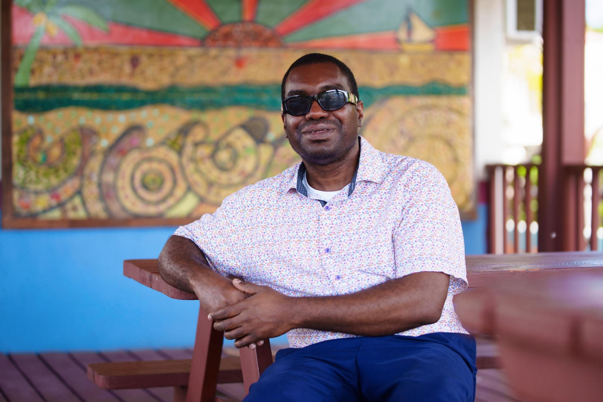 Kevin E. Cartwright seated at a wooden table with colourful Bahamian-style artwork in the background.